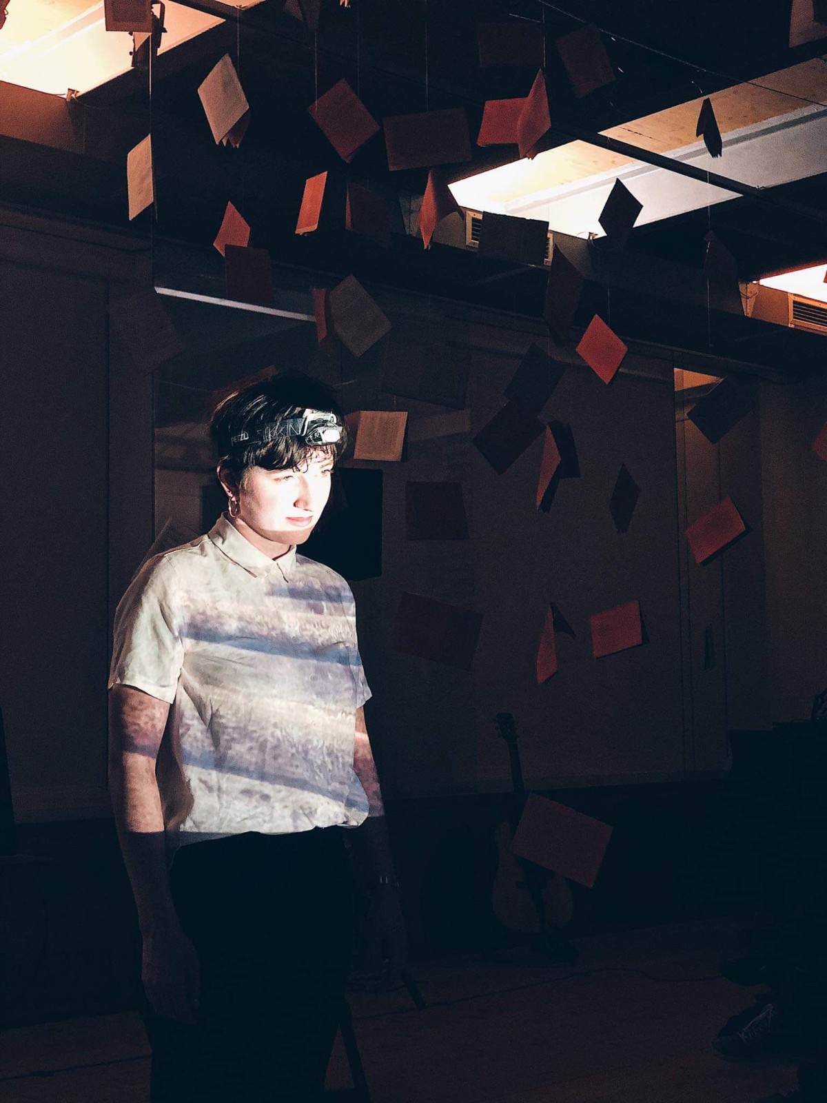 Eine Schauspielerin steht in einem dunklen Raum und wird von einem hellen Licht angestrahlt.