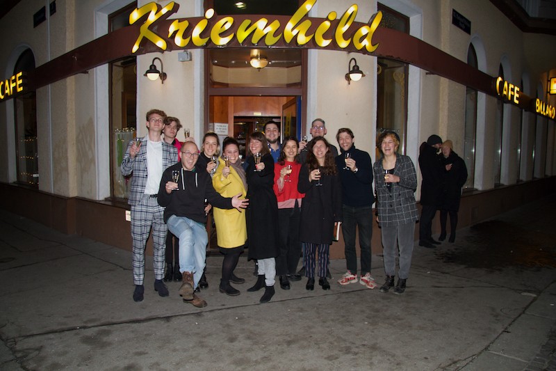 Eine Gruppe Studierender steht vor dem Cafe Kriemhild und lächelt und hält ihre Gläser hoch.